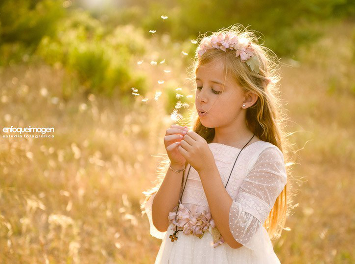 Niña de Primera Comunión soplando una flor durante una sesión en exterior